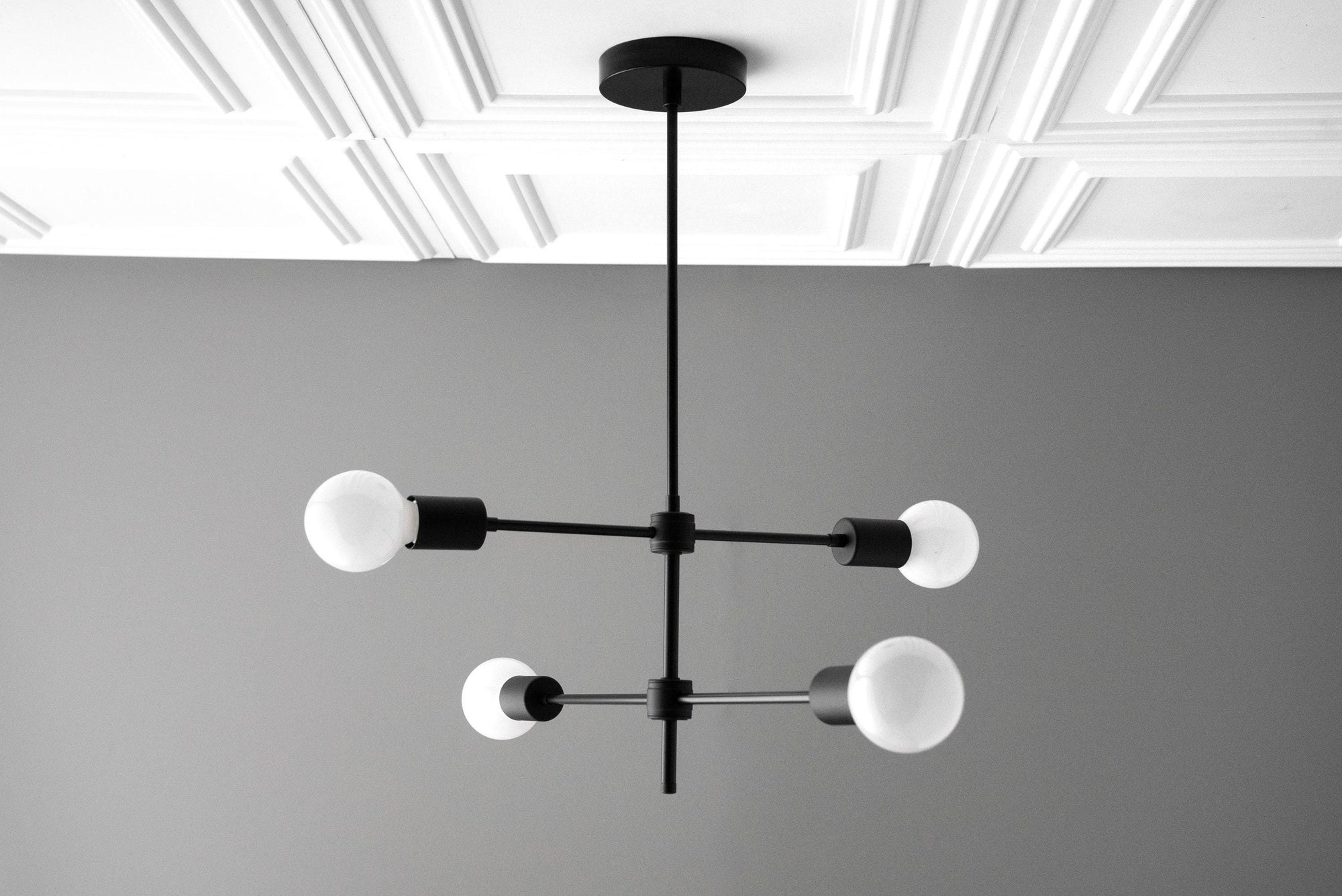 Black metal Art Deco chandelier with four frosted globe bulbs and horizontal and vertical arms. - CHANDELIER MODEL NO. 5598