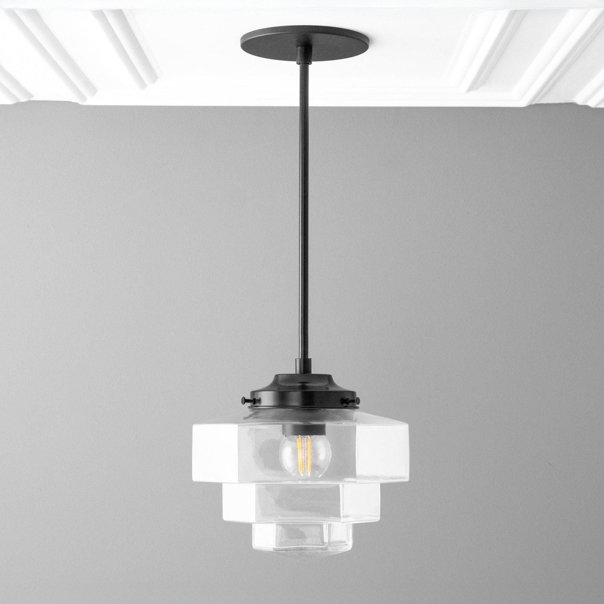 Modern pendant light with clear glass shade and black fixture on a gray background