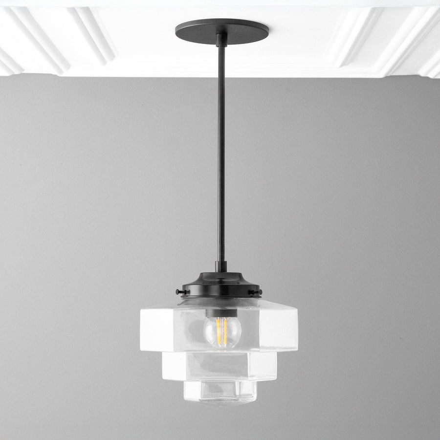 Modern pendant light with clear glass shade and black fixture on a gray background