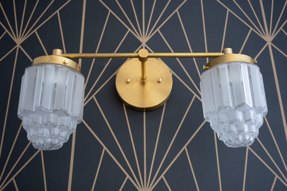 Raw brass 2-bulb vanity light with fluted glass globes and round wall mount against geometric wallpaper. - VANITY LIGHT MODEL NO. 9777