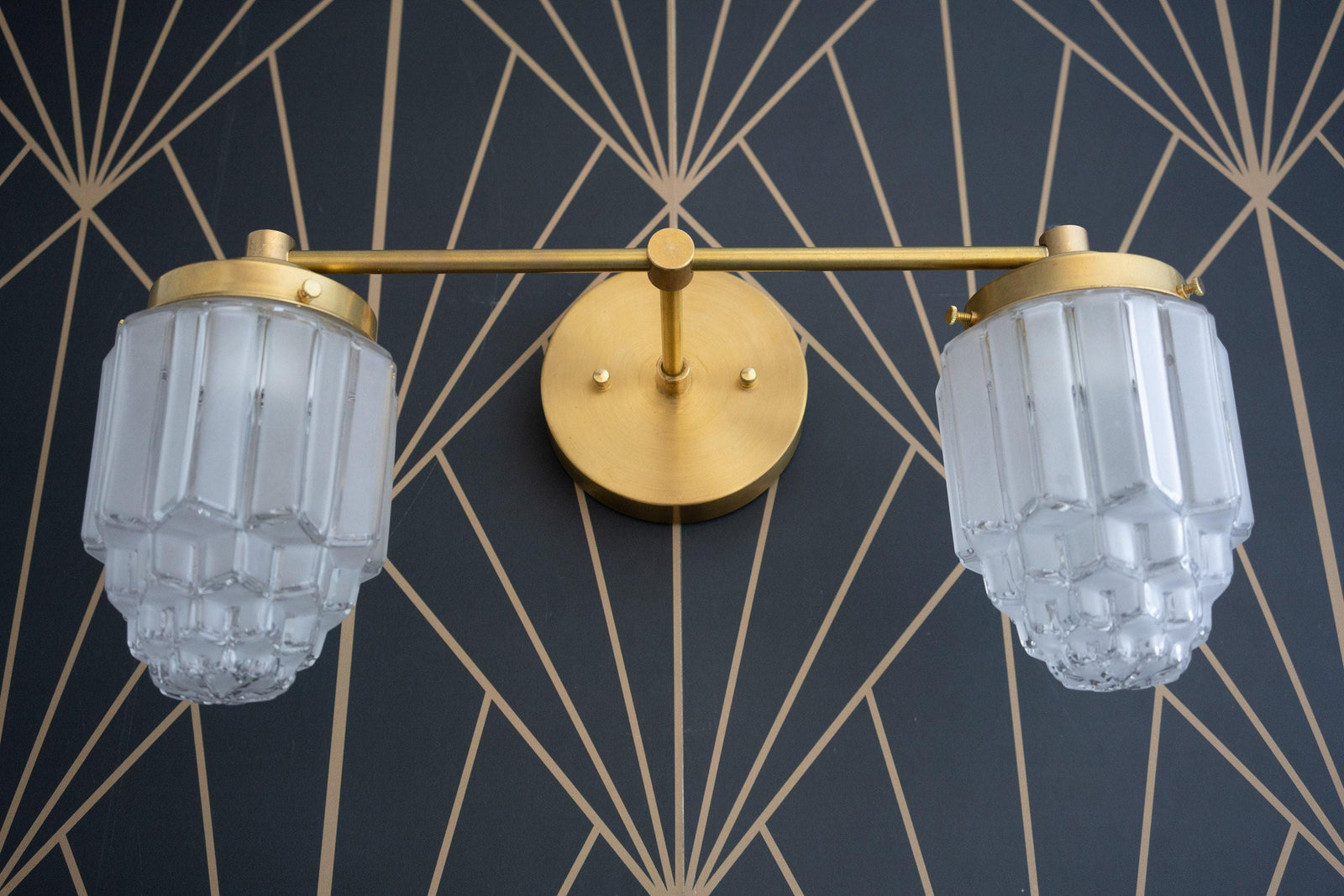 Raw brass 2-bulb vanity light with fluted glass globes and round wall mount against geometric wallpaper. - VANITY LIGHT MODEL NO. 9777