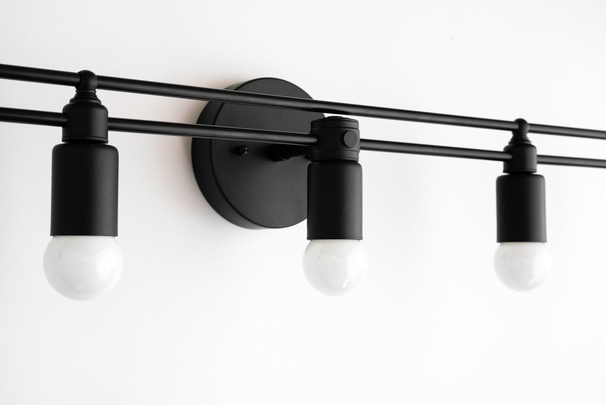 Black metal vanity light fixture with three exposed bulbs and round wall mount. - VANITY LIGHT MODEL NO. 3933