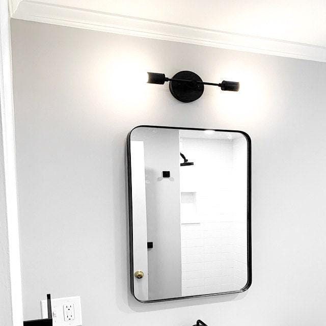 Art Deco style vanity light with black cylindrical shades and round black wall mount above rectangular mirror with rounded. - VANITY LIGHT MODEL NO. 8057