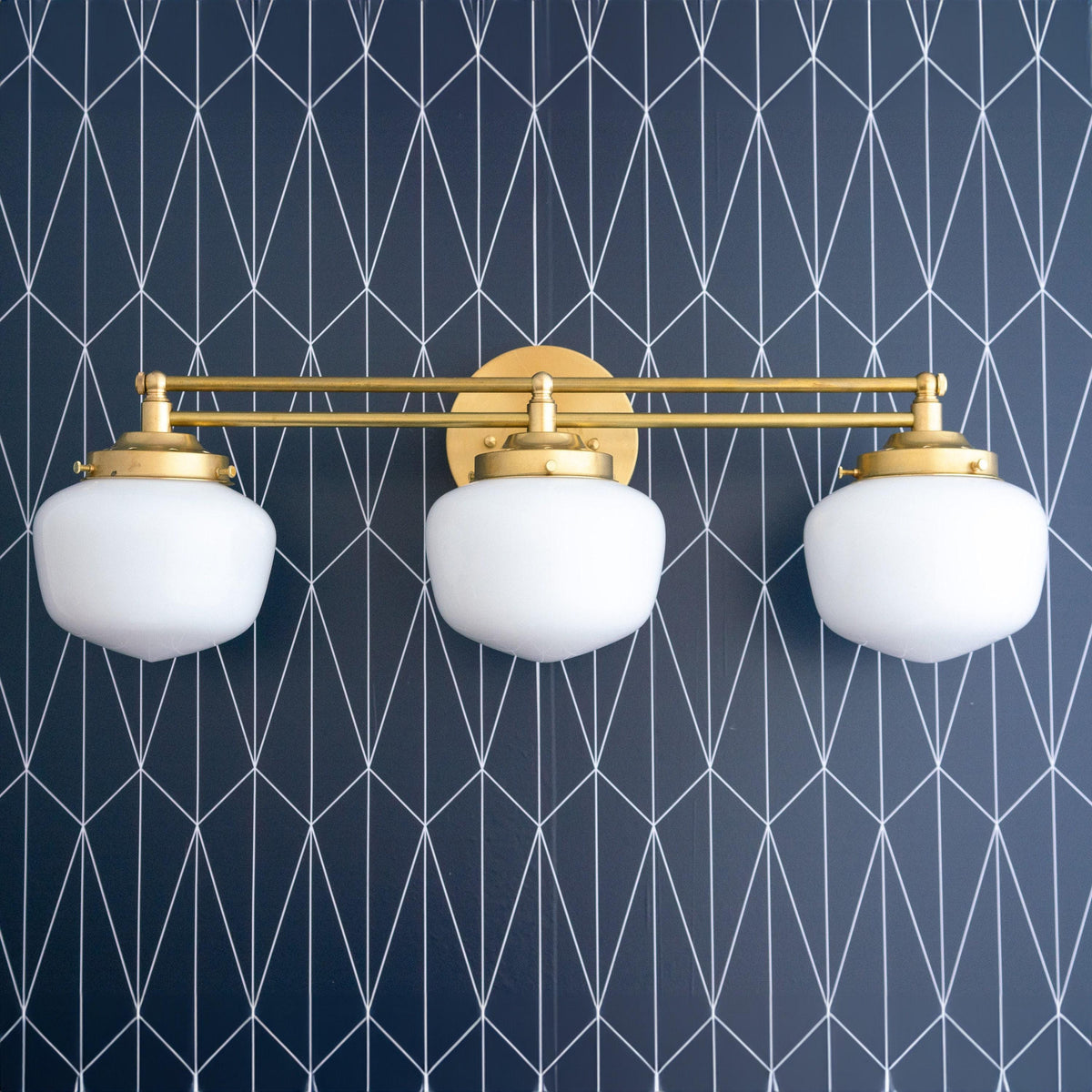 Art Deco 3-bulb vanity light in polished brass with white globe shades against navy geometric wall. - VANITY LIGHT MODEL NO. 4352