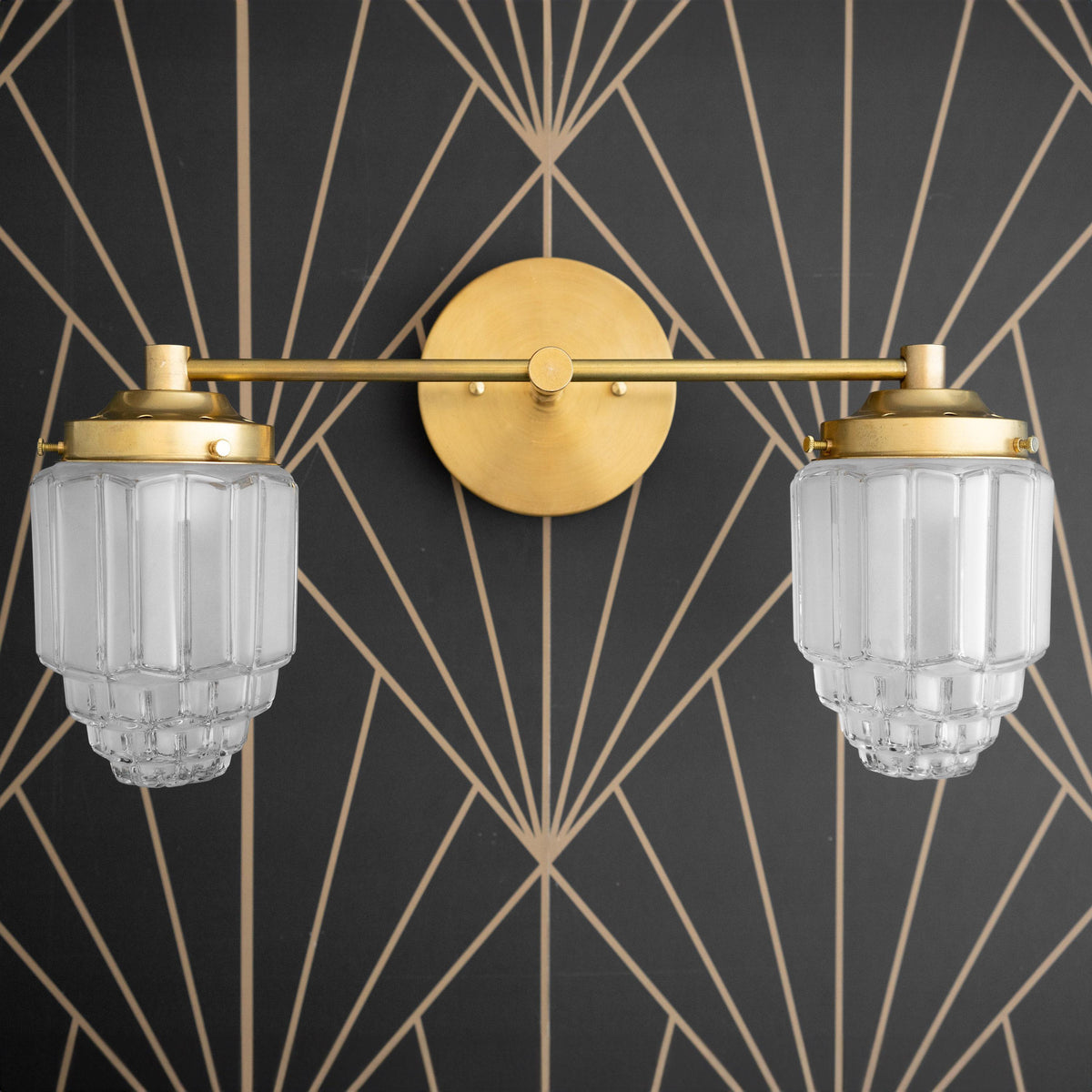 Two-bulb vanity light with raw brass finish and textured globe glass shades mounted on geometric black and gold wall. - VANITY LIGHT MODEL NO. 9777
