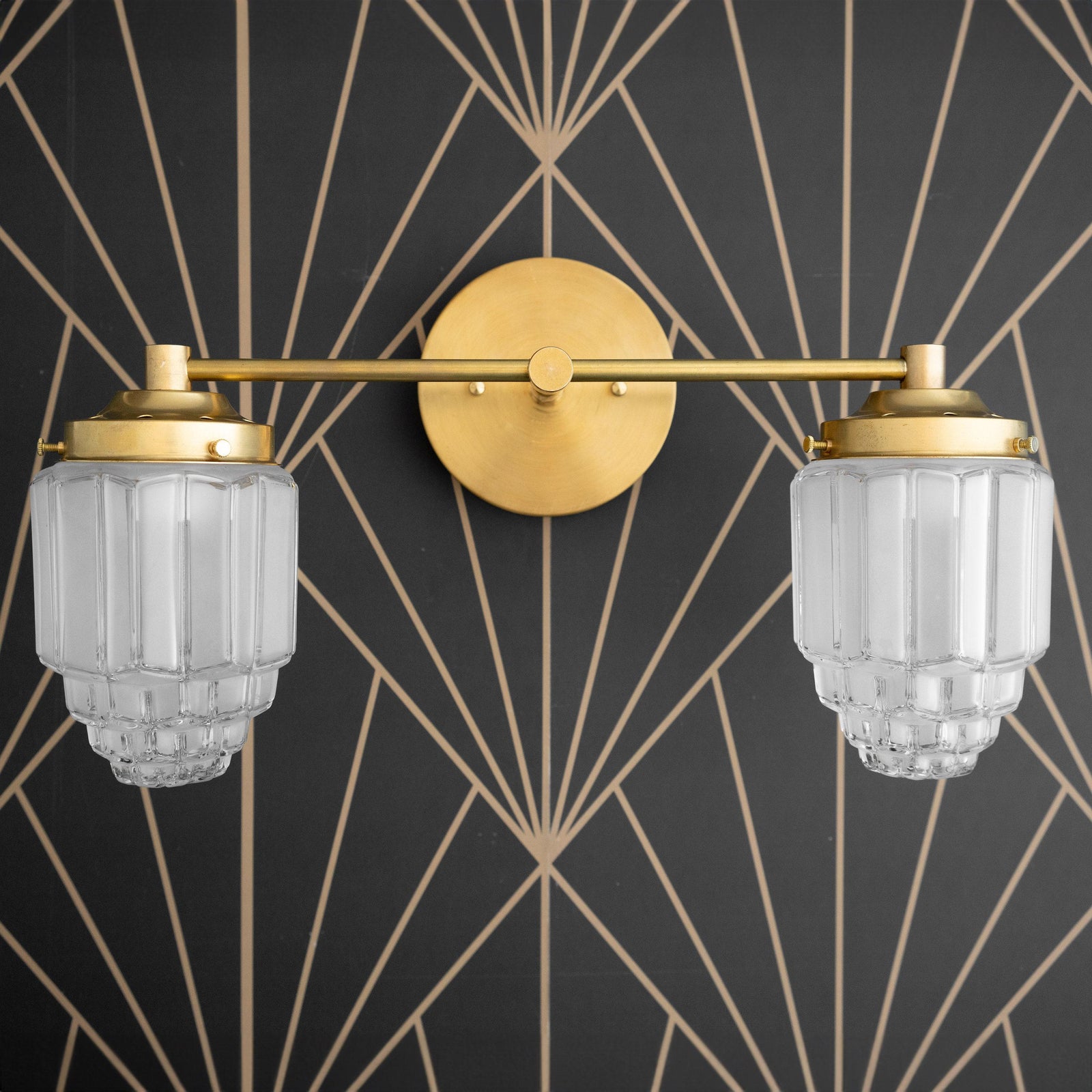 Two-bulb vanity light with raw brass finish and textured globe glass shades mounted on geometric black and gold wall. - VANITY LIGHT MODEL NO. 9777