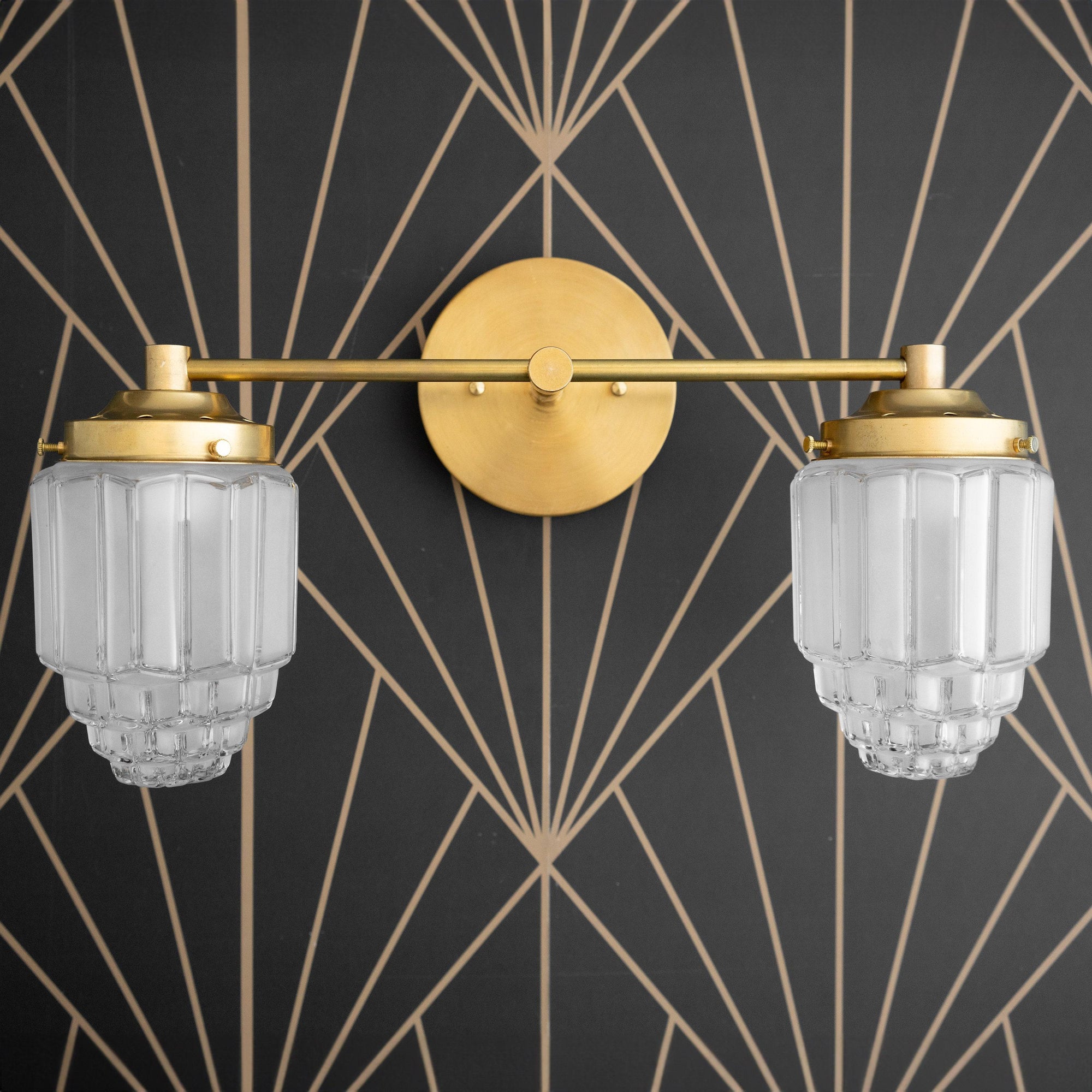 Two-bulb vanity light with raw brass finish and textured globe glass shades mounted on geometric black and gold wall. - VANITY LIGHT MODEL NO. 9777