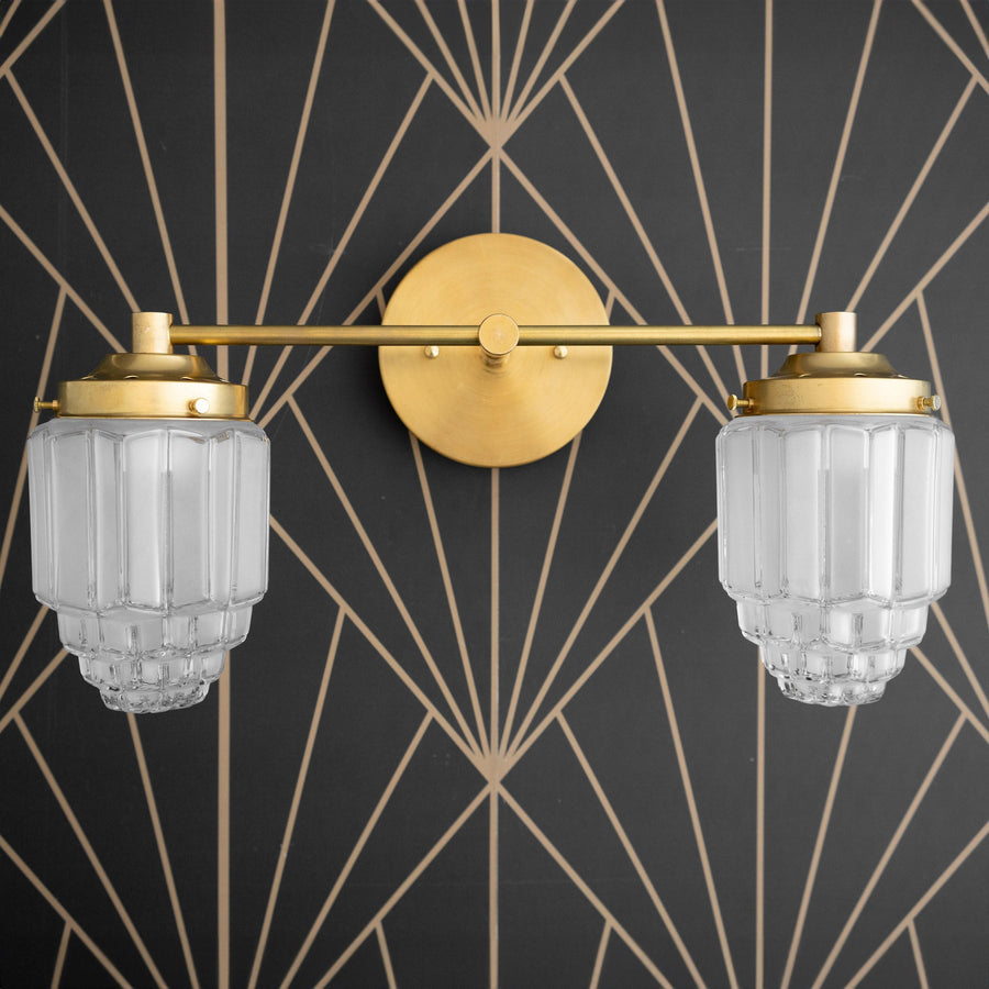 Two-bulb vanity light with raw brass finish and textured globe glass shades mounted on geometric black and gold wall. - VANITY LIGHT MODEL NO. 9777