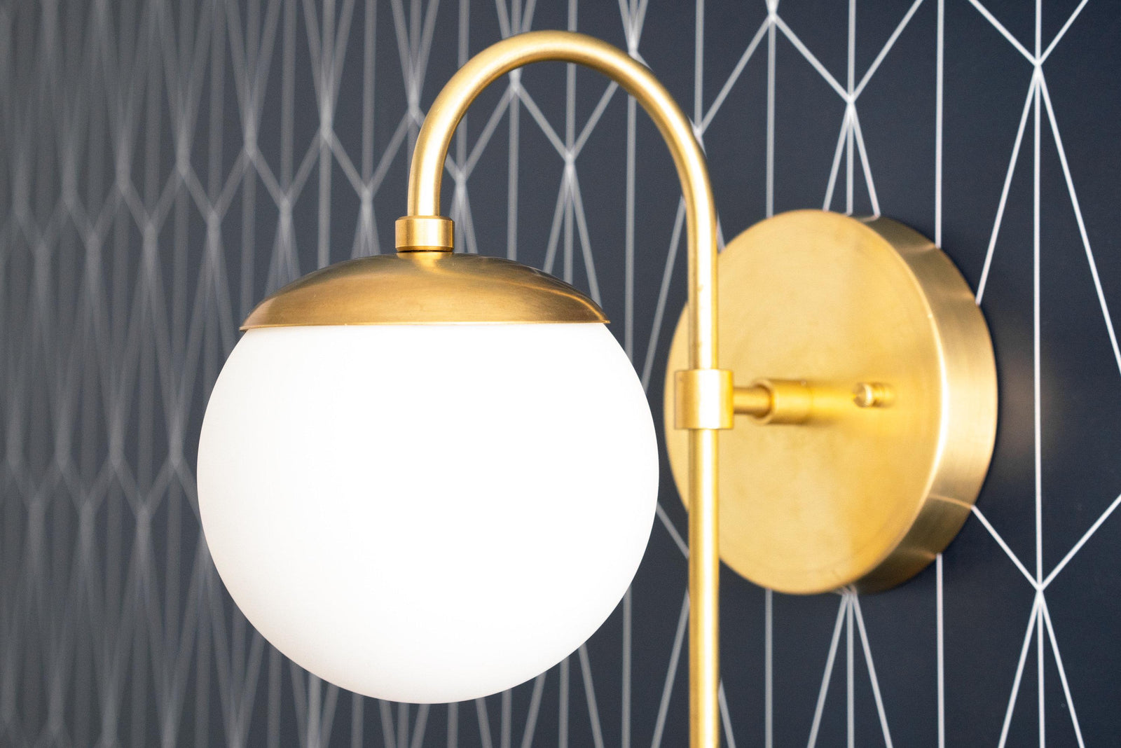 Art Deco brass wall sconce with frosted white globe and curved arm against geometric wallpaper. - SCONCE MODEL NO. 1045