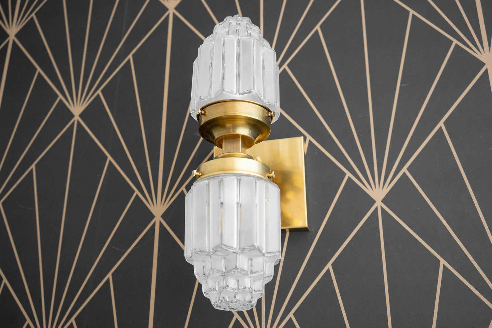 Art Deco style wall sconce with frosted glass globe and polished brass fixture on geometric black and gold background. - SCONCE MODEL NO. 7180