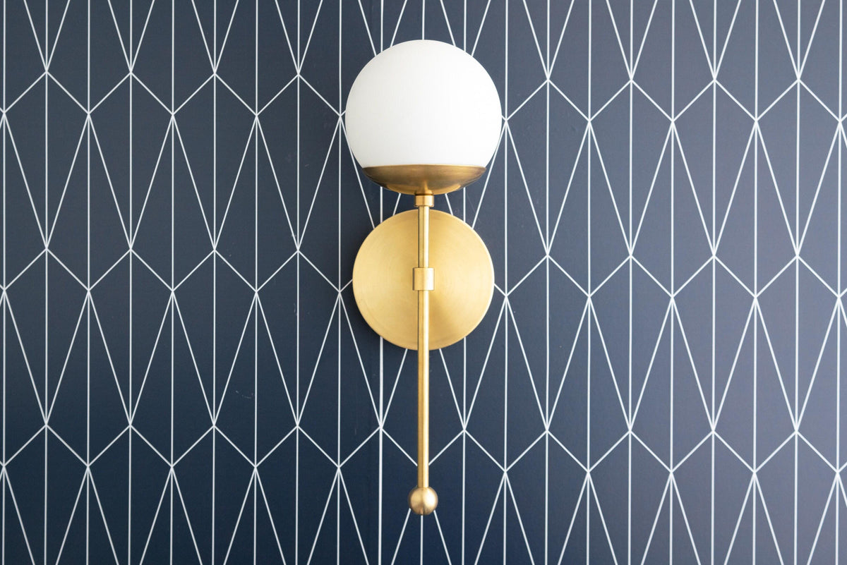 Art Deco wall sconce with round white globe shade and polished brass finish on geometric dark blue wall. - SCONCE MODEL NO. 1048