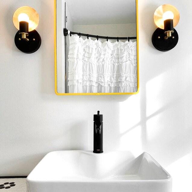 Pair of brass and black Art Deco bare bulb wall sconces flanking a yellow-framed mirror above a white sink. - SCONCE MODEL NO. 8677