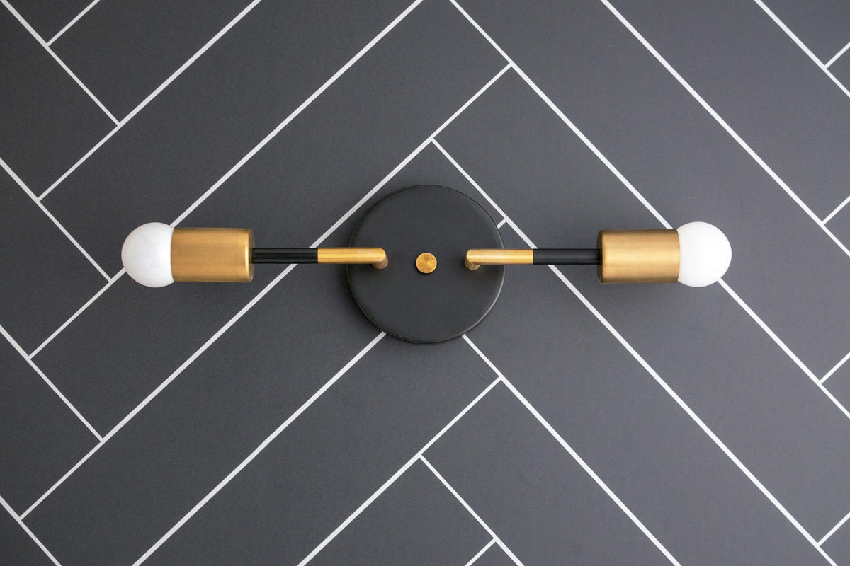 Raw brass and matte black 2-bulb Art Deco vanity light with exposed round bulbs on herringbone tile wall. - VANITY LIGHT MODEL NO. 1938