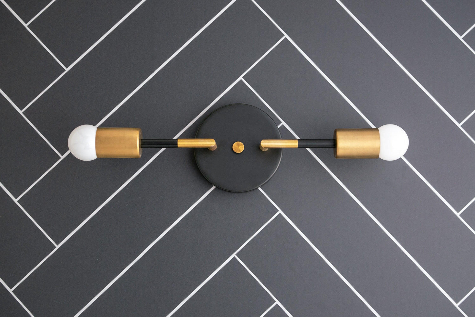 Raw brass and matte black 2-bulb Art Deco vanity light with exposed round bulbs on herringbone tile wall. - VANITY LIGHT MODEL NO. 1938