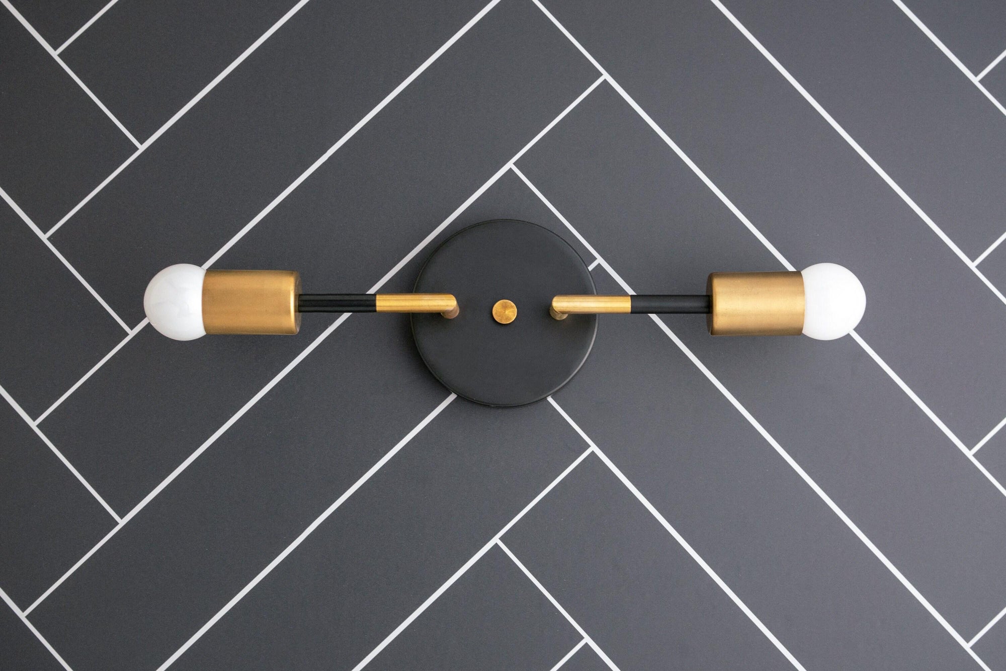 Raw brass and matte black 2-bulb Art Deco vanity light with exposed round bulbs on herringbone tile wall. - VANITY LIGHT MODEL NO. 1938