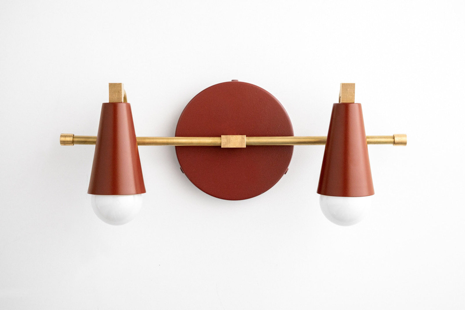 Two-bulb vanity light with raw brass finish and brick red conical shades on a round wall mount. - VANITY LIGHT MODEL NO. 1229