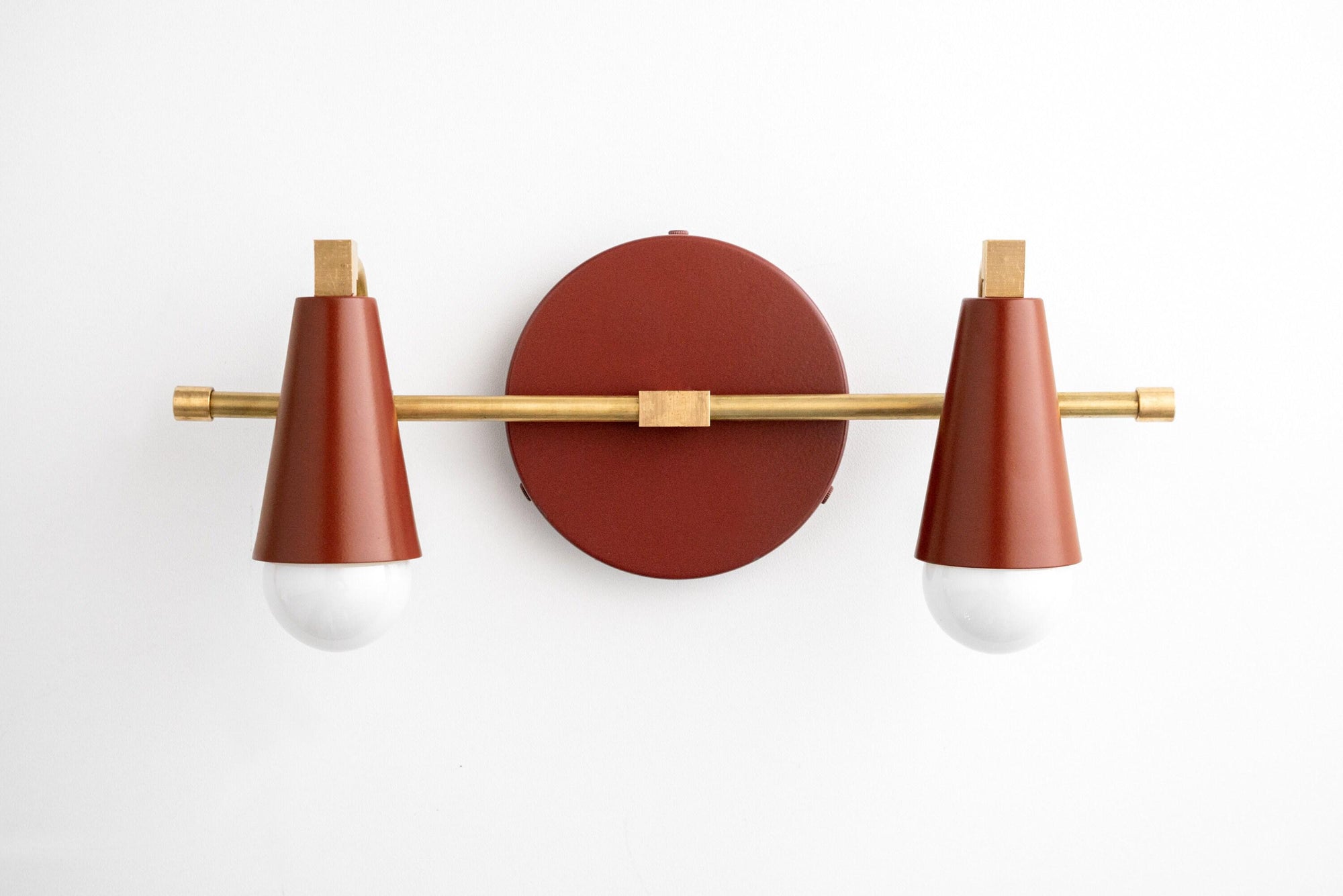 Two-bulb vanity light with raw brass finish and brick red conical shades on a round wall mount. - VANITY LIGHT MODEL NO. 1229
