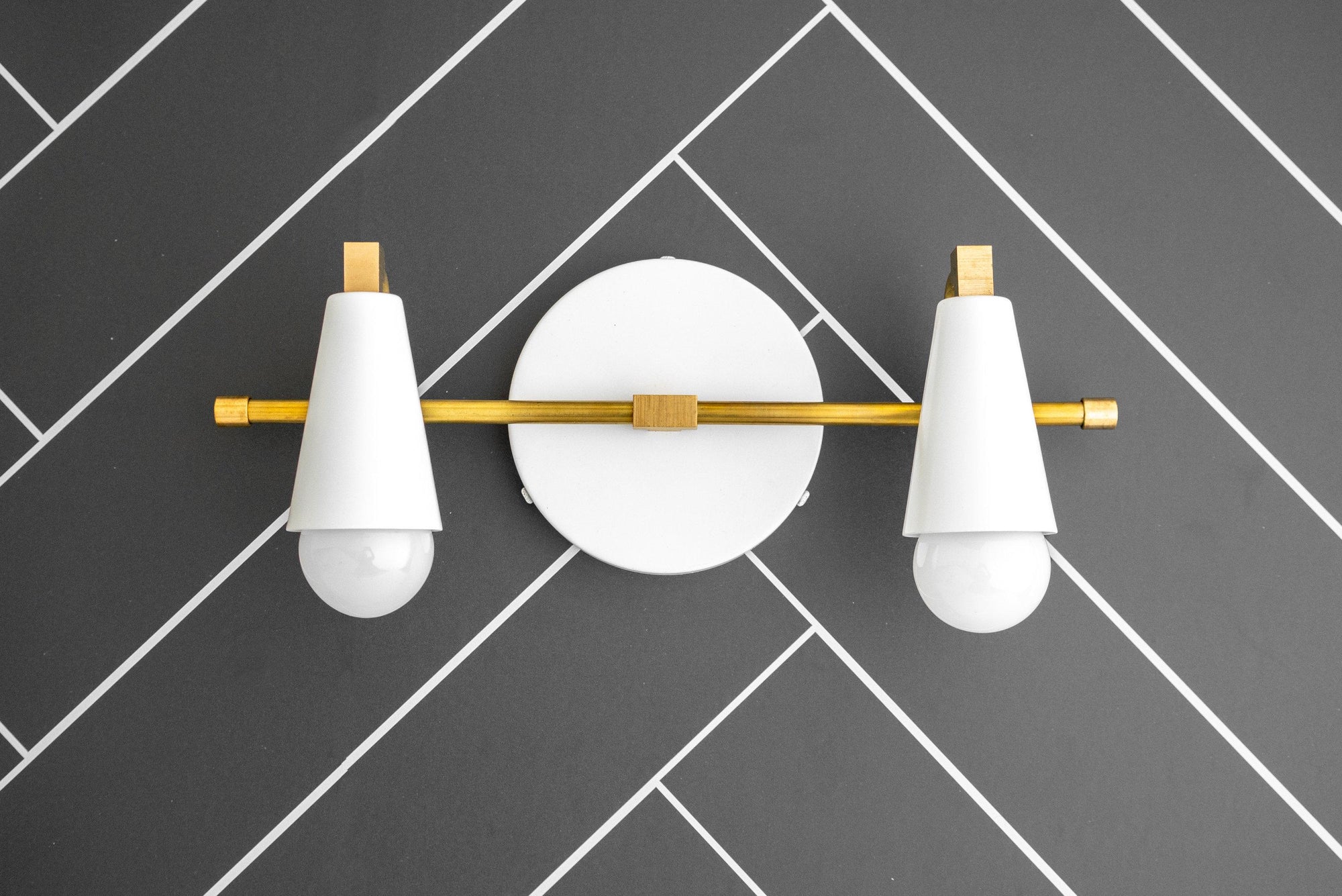 Raw brass two-bulb vanity light with matte white tapered shades mounted on black tiled wall. - VANITY LIGHT MODEL NO. 1229