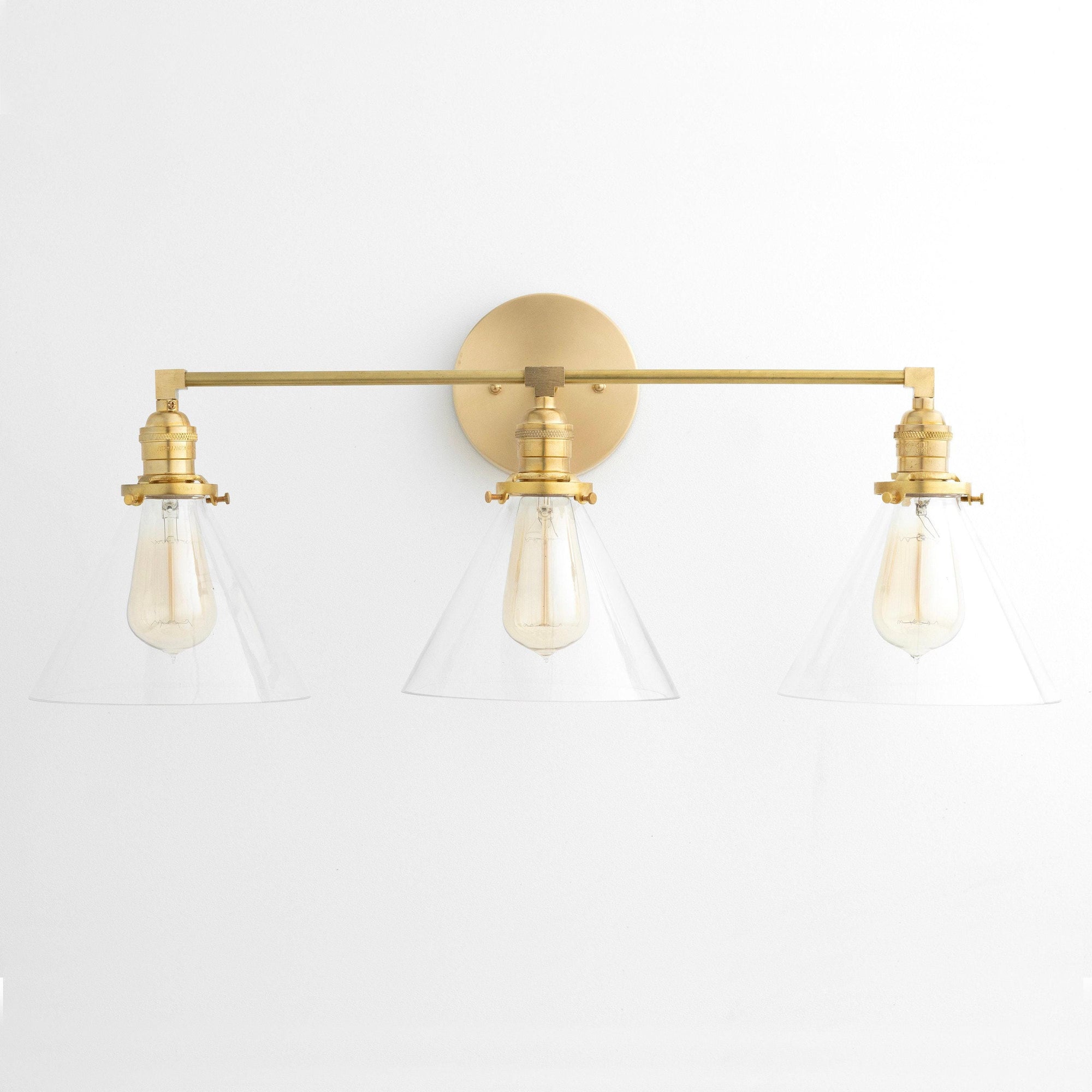 Mid-century modern 3-bulb vanity light with raw brass finish and clear glass conical shades. - VANITY LIGHT MODEL NO. 5219