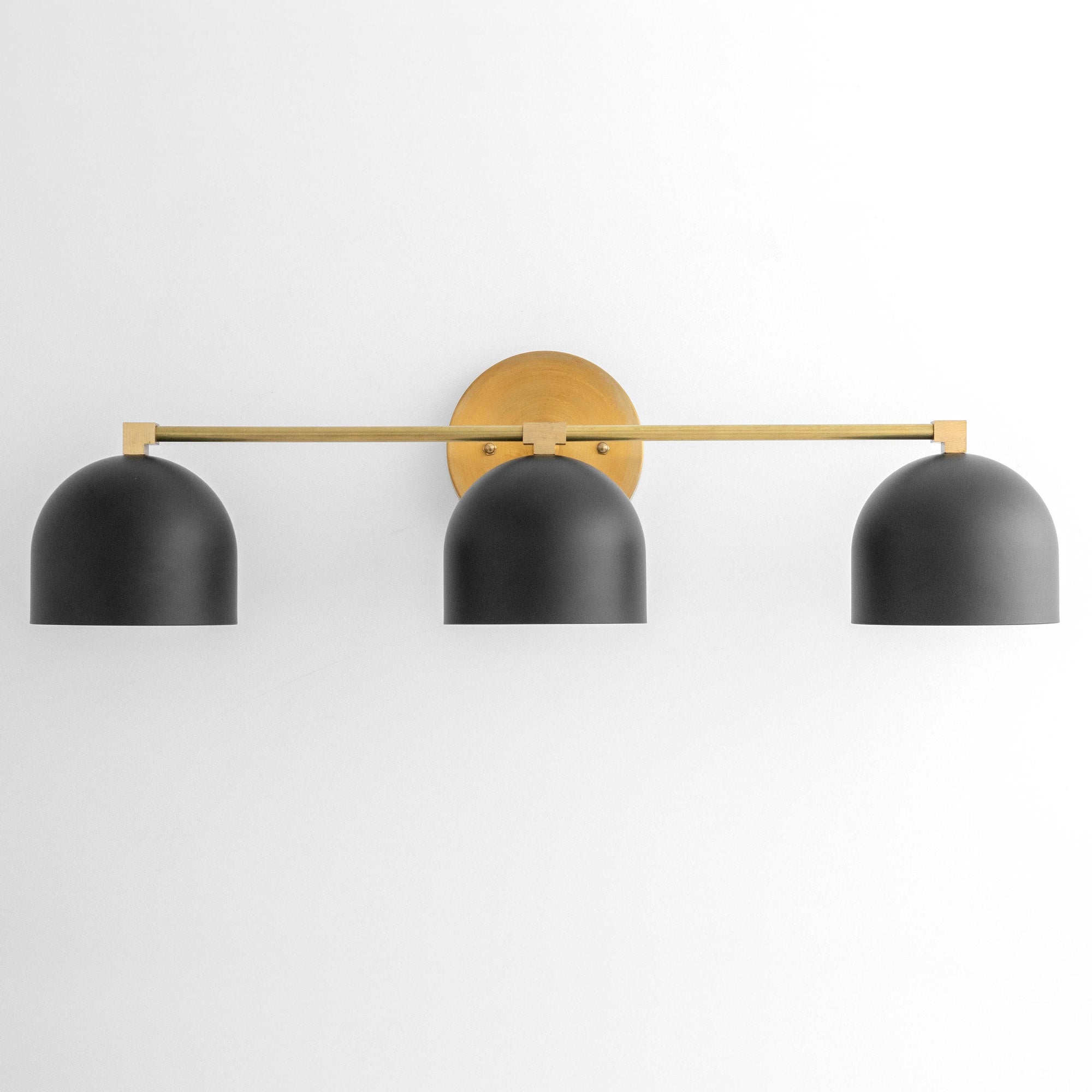 Three-bulb vanity light with black dome shades and brass horizontal bar mounting on wall. - VANITY LIGHT MODEL NO. 7565