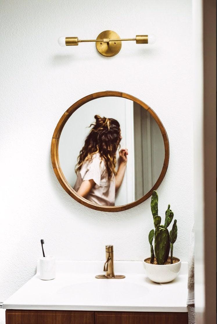 Mid-century modern vanity light in raw brass with two exposed bulbs above a round wooden mirror. - VANITY LIGHT MODEL NO. 5563