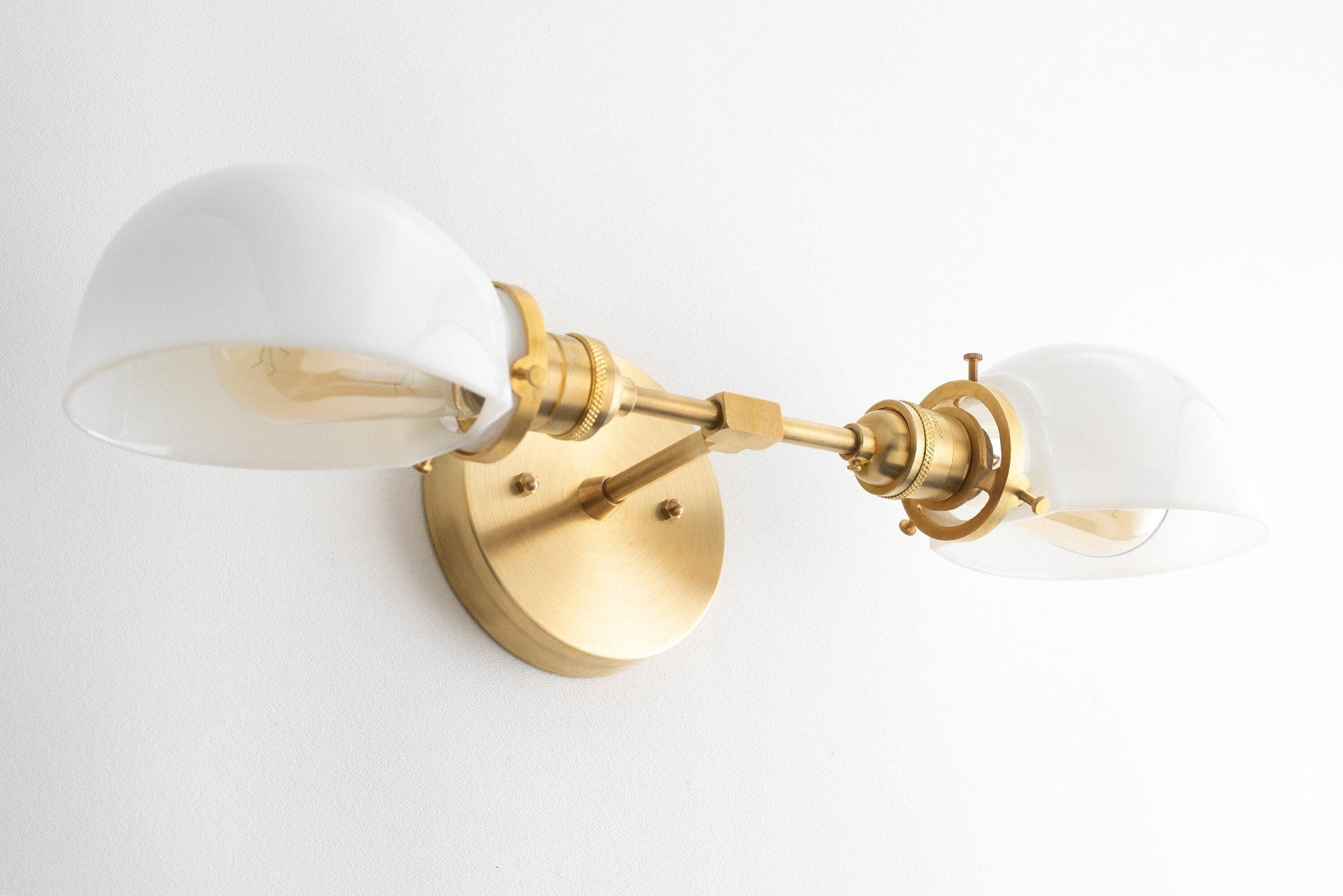 Two-bulb vanity light with antique brass finish and white curved glass shades mounted on a round wall plate. - VANITY LIGHT MODEL NO. 1734