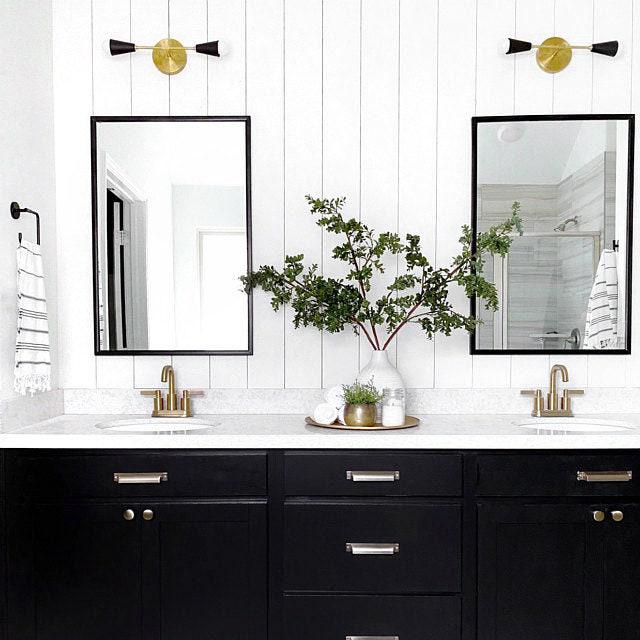 Mid-century modern 2-bulb vanity light in raw brass with black accents above dual black-framed mirrors. - VANITY LIGHT MODEL NO. 3209