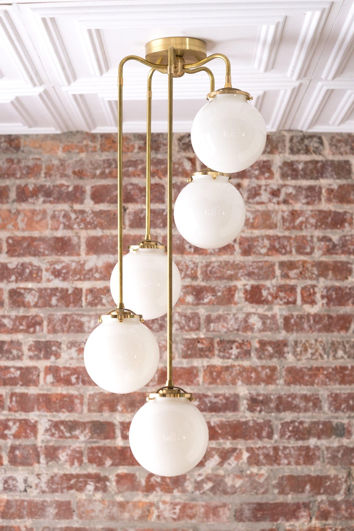 Mid-century modern chandelier with five frosted glass globes and raw brass finish against a brick wall background. - CHANDELIER MODEL NO. 1809