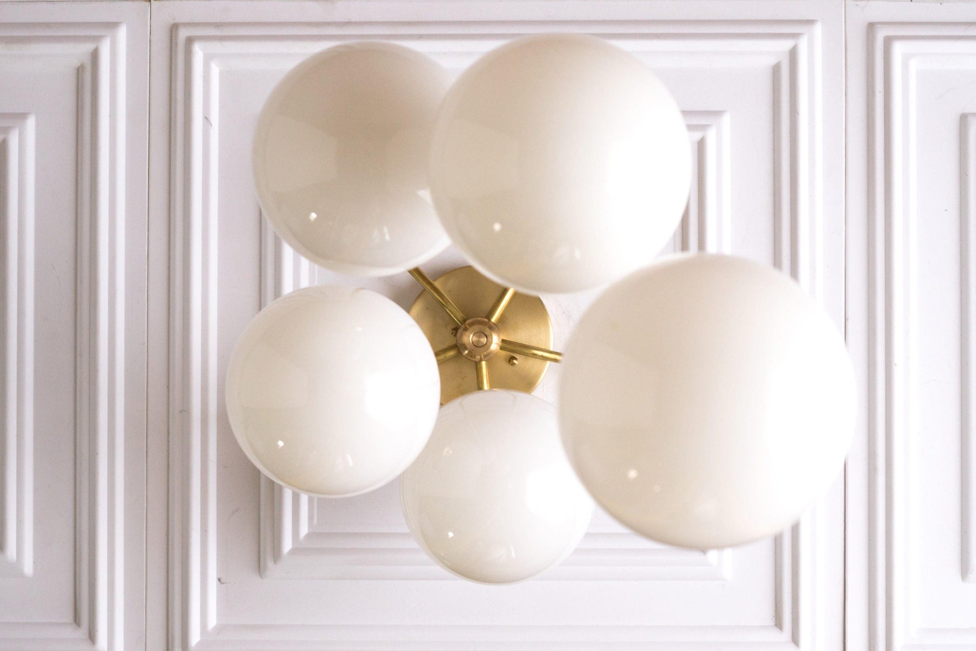 Mid-century modern chandelier with five white globe lights and raw brass fixtures against white paneled wall. - CHANDELIER MODEL NO. 1809
