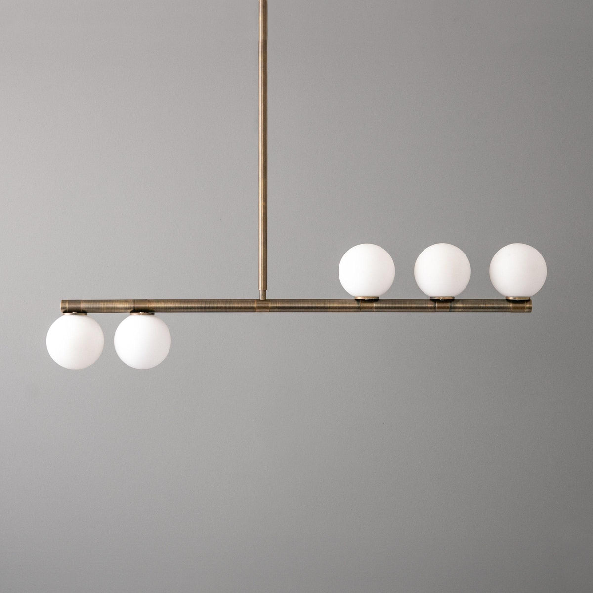 Mid-century modern linear chandelier with antique brass finish and five white globe lights. - CHANDELIER MODEL NO. 6507