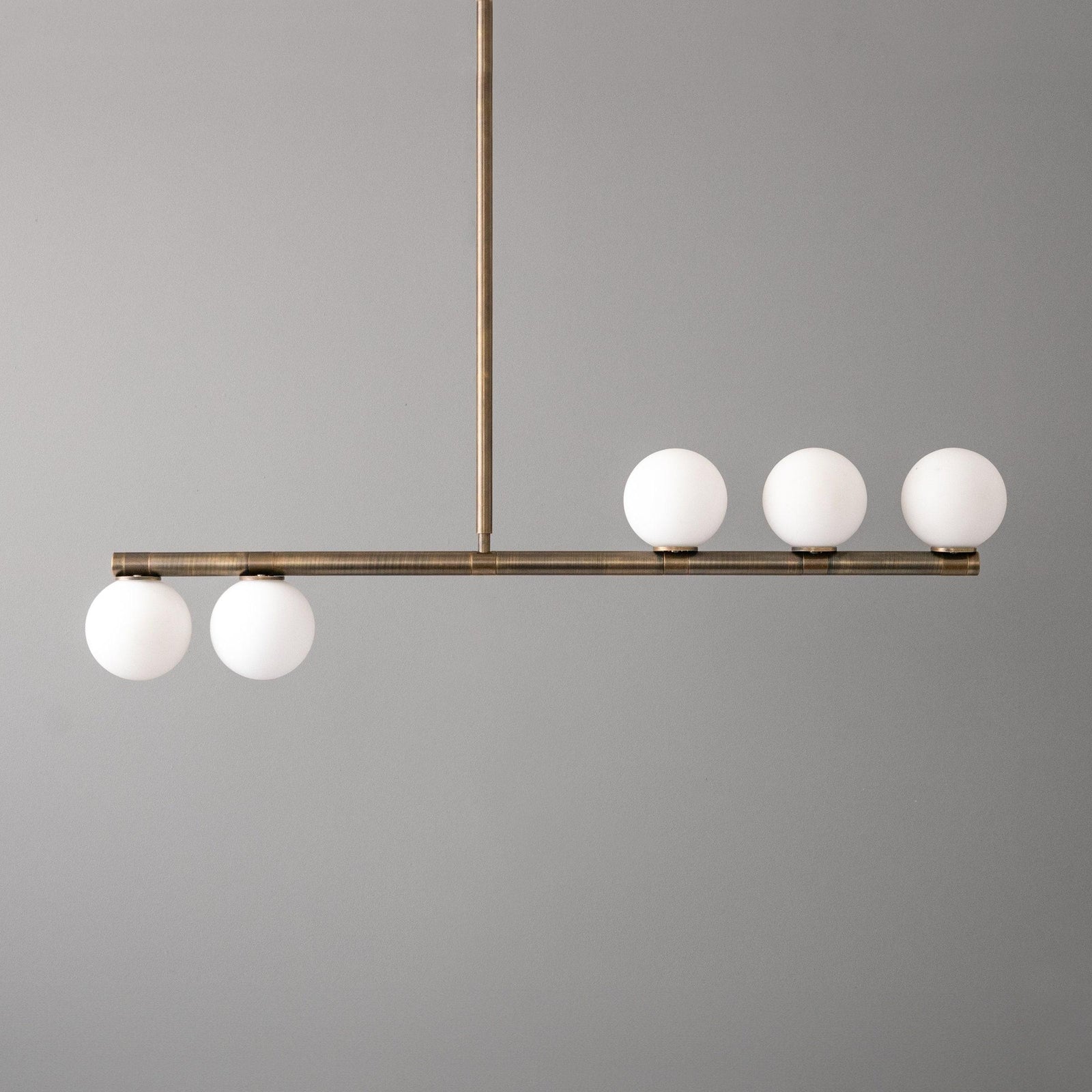 Mid-century modern linear chandelier with antique brass finish and five white globe lights. - CHANDELIER MODEL NO. 6507