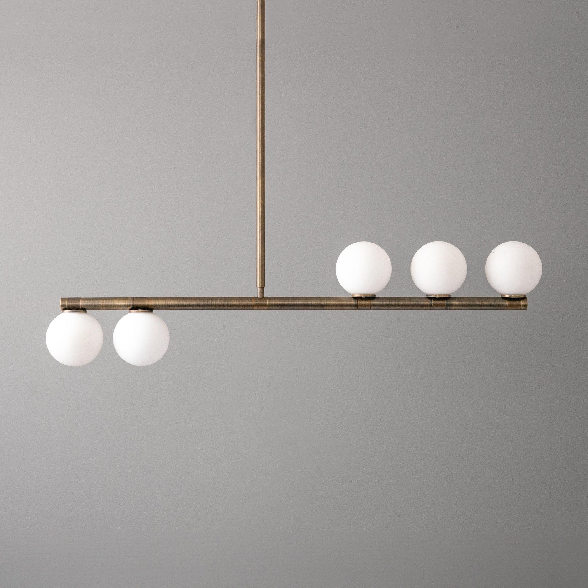 Mid-century modern linear chandelier with antique brass finish and five white globe lights. - CHANDELIER MODEL NO. 6507