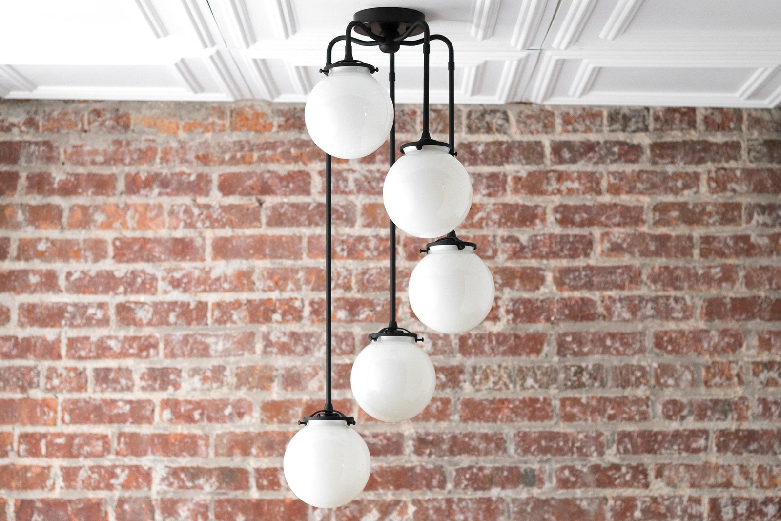 Mid-century modern black chandelier with five white globe shades hanging at staggered heights against a brick wall. - CHANDELIER MODEL NO. 1809