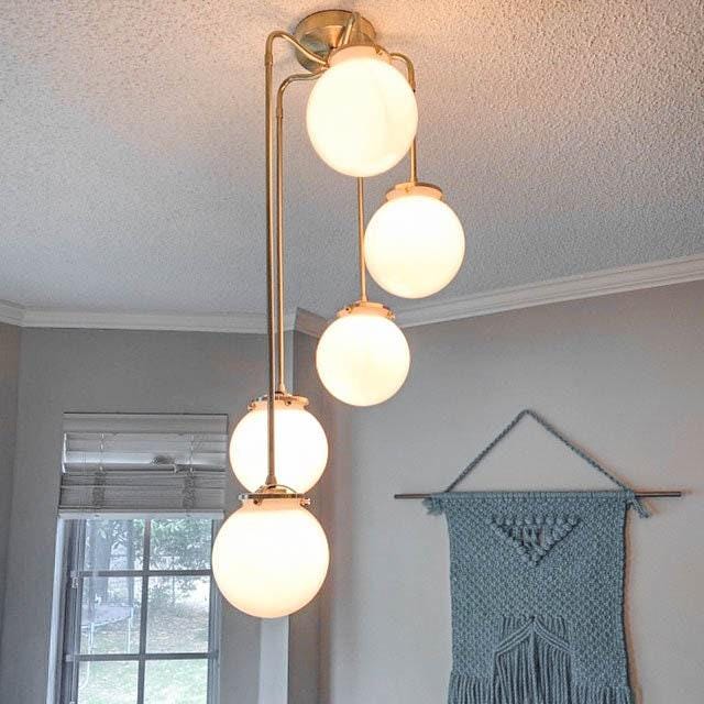 Mid-century modern chandelier with five glowing white globe lights and sealed brass finish suspended in a living room. - CHANDELIER MODEL NO. 1809