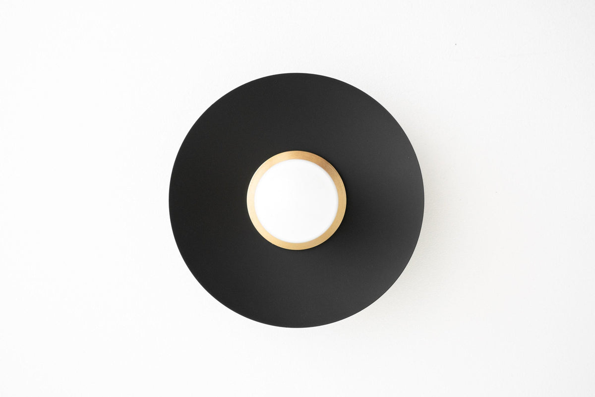 Black circular wall sconce with a central bare bulb and brass ring detail. - SCONCE MODEL NO. 7004