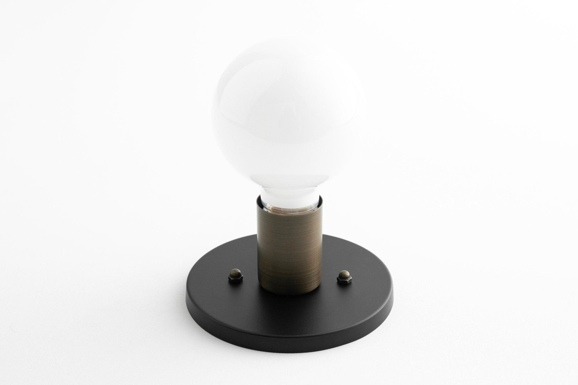 Mid-century modern black flush sconce with bare bulb and cylindrical brass holder on round base. - SCONCE MODEL NO. 2057