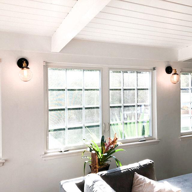 Pair of mid-century modern black and raw brass globe sconces mounted on white walls beside large windows with a vaulted. - SCONCE MODEL NO. 5456