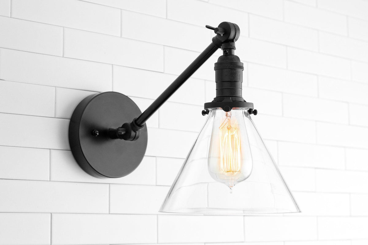 Black adjustable wall sconce with clear glass cone shade and exposed filament bulb on white tile wall. - SCONCE MODEL NO. 7962