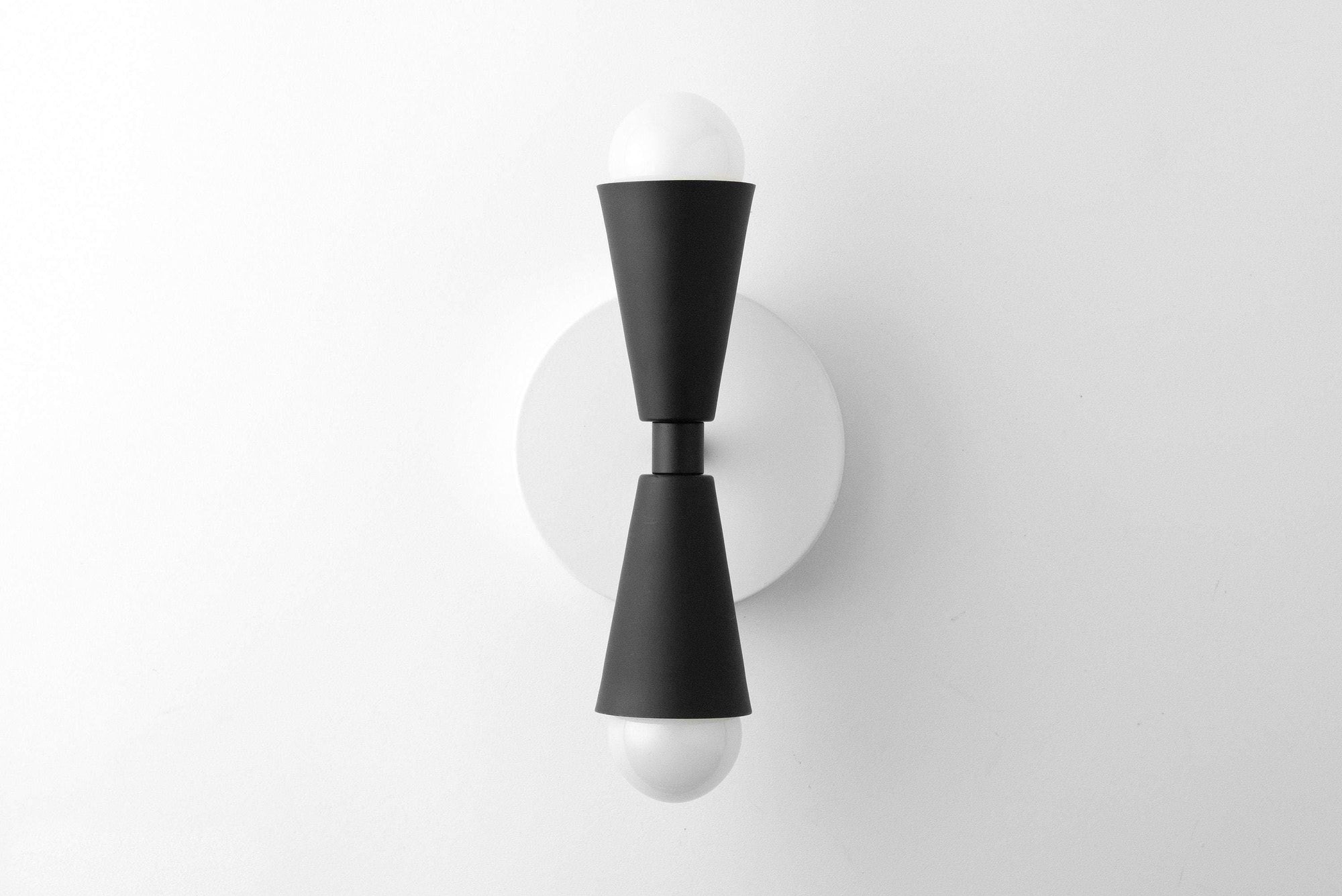 Mid-century modern black metal sconce with bare bulbs at both ends and round wall mount. - SCONCE MODEL NO. 4717