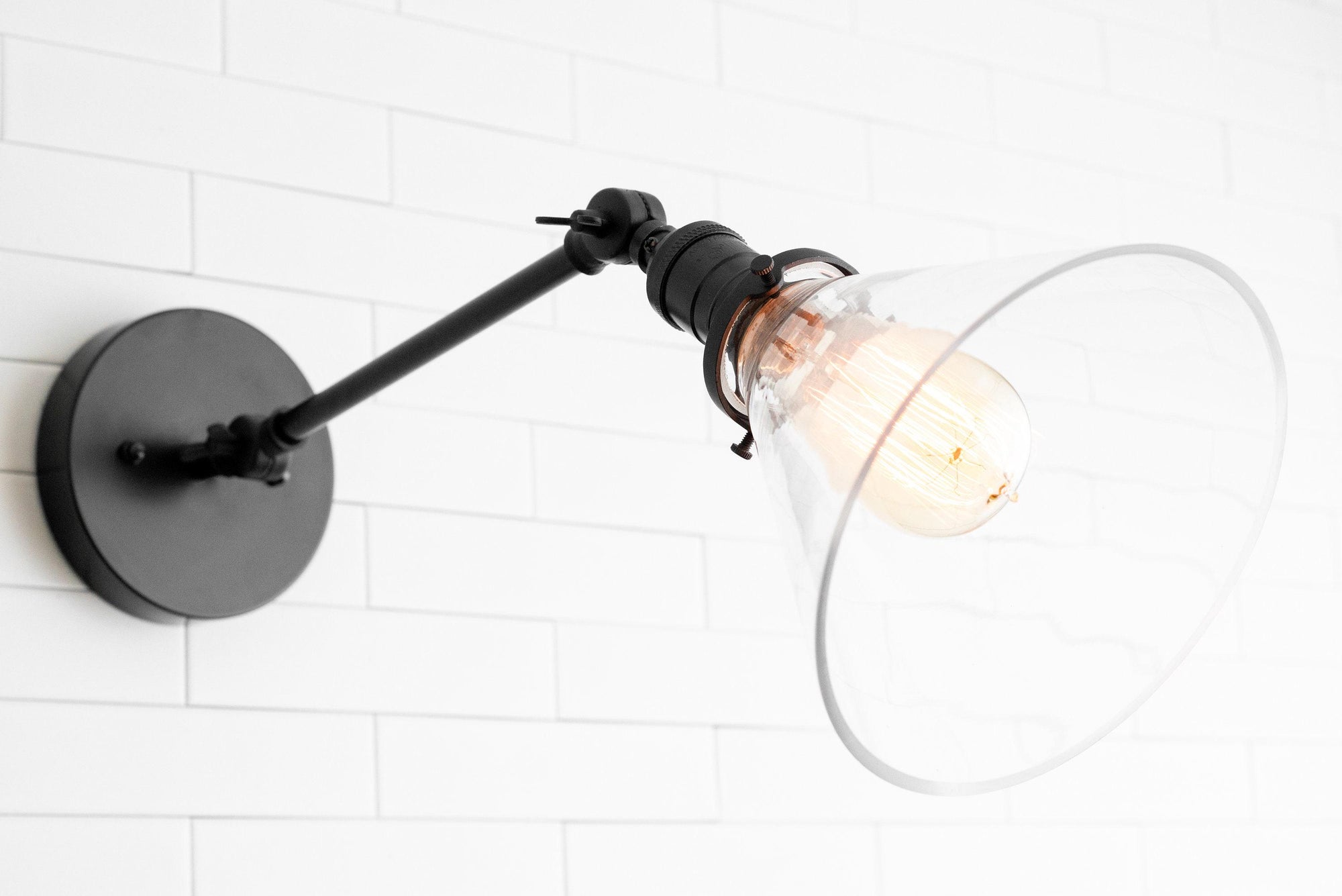 Adjustable black metal wall sconce with clear glass shade and exposed bulb on white tiled background. - SCONCE MODEL NO. 7962