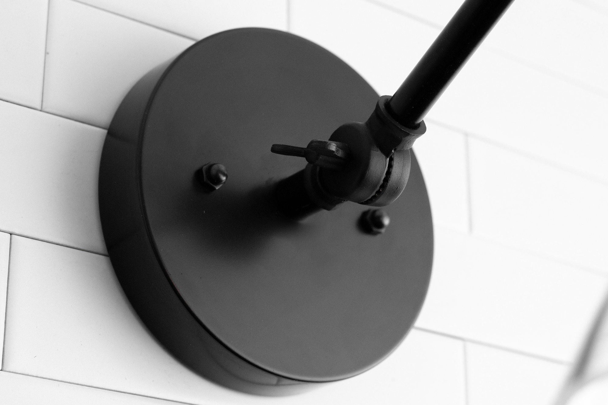 Matte black adjustable wall sconce mount with round base and swivel joint on white tiled wall. - SCONCE MODEL NO. 7962
