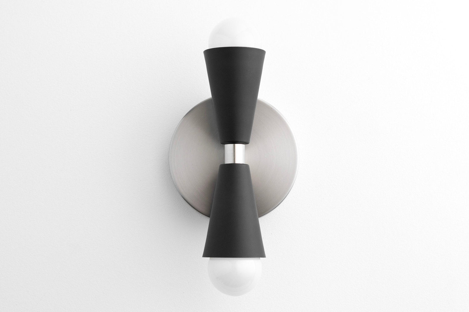 Mid-century modern up/down sconce with brushed nickel base and black tapered cylindrical shades housing exposed bulbs. - SCONCE MODEL NO. 4717