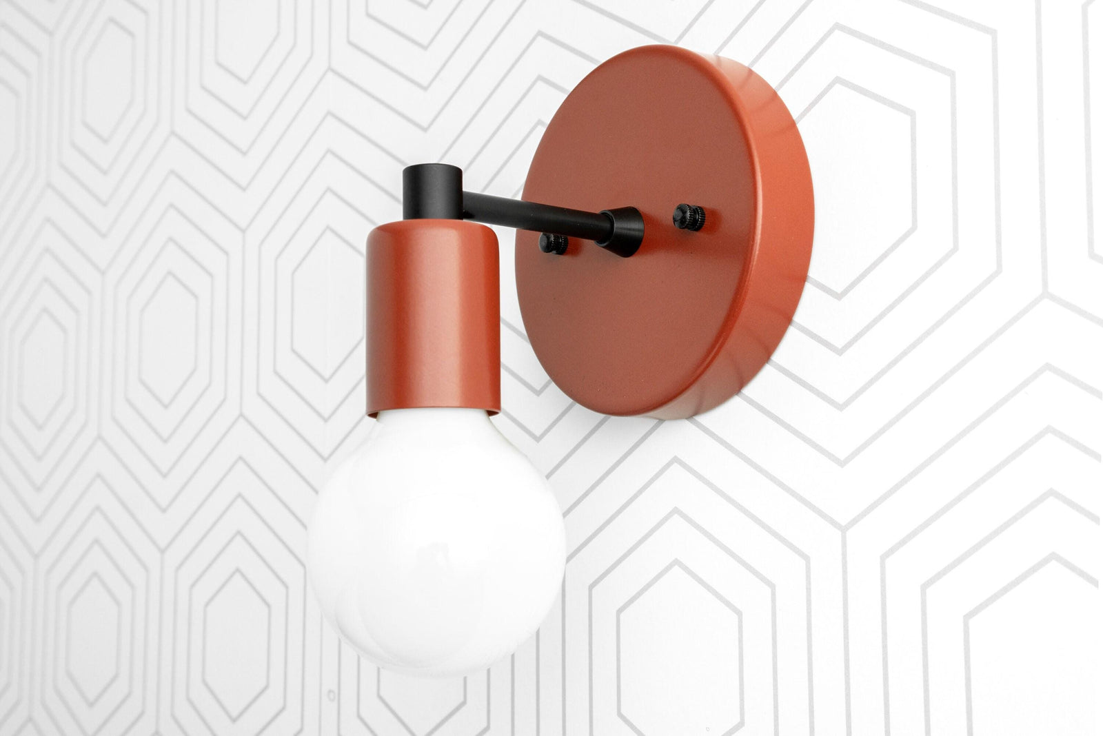 Scandinavian-style wall sconce in matte orange with exposed bulb and black arm on white geometric wall. - SCONCE MODEL NO. 9036
