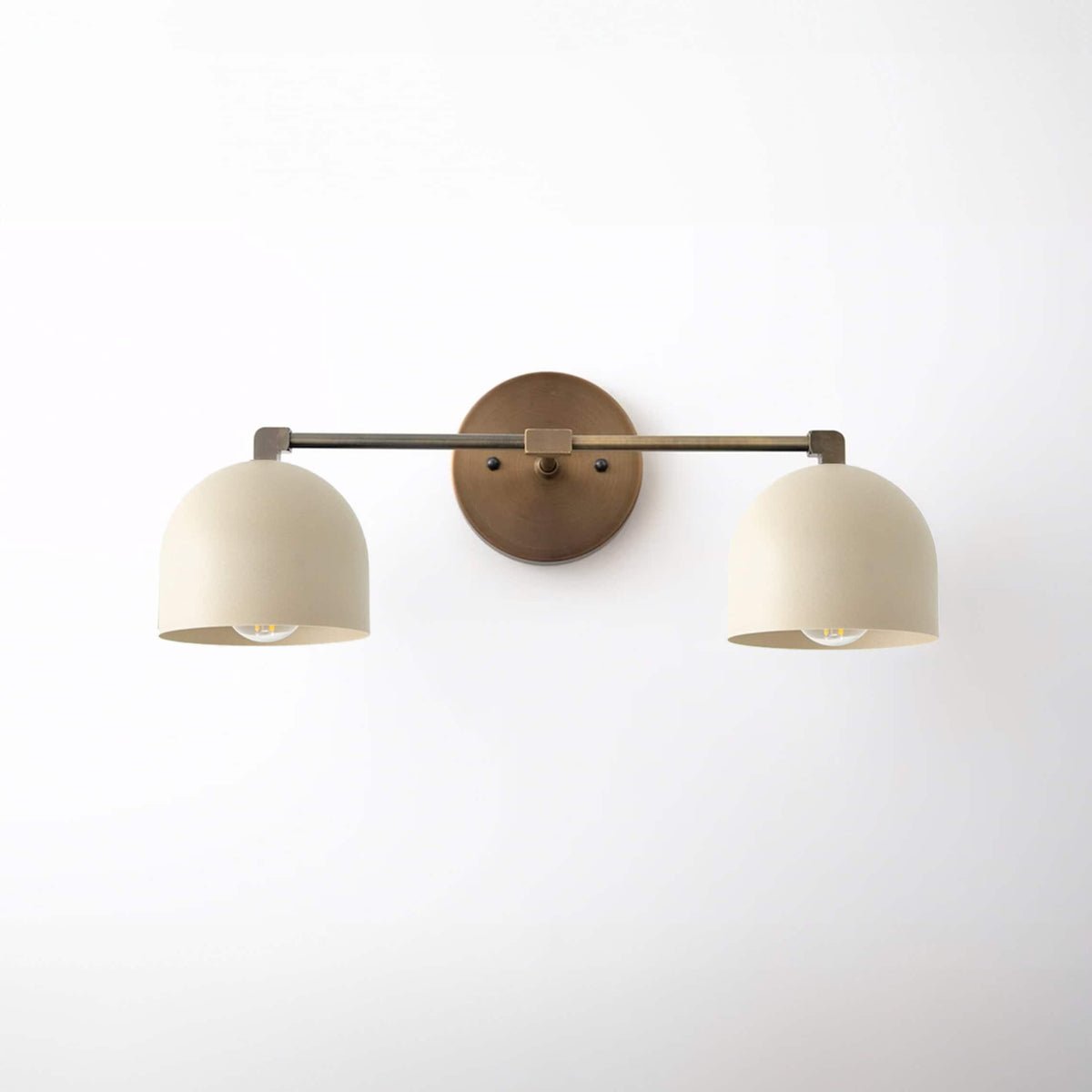 Two-light vanity fixture with antique brass finish and cream-colored dome shades in a minimalist style. - VANITY LIGHT MODEL NO. 0698