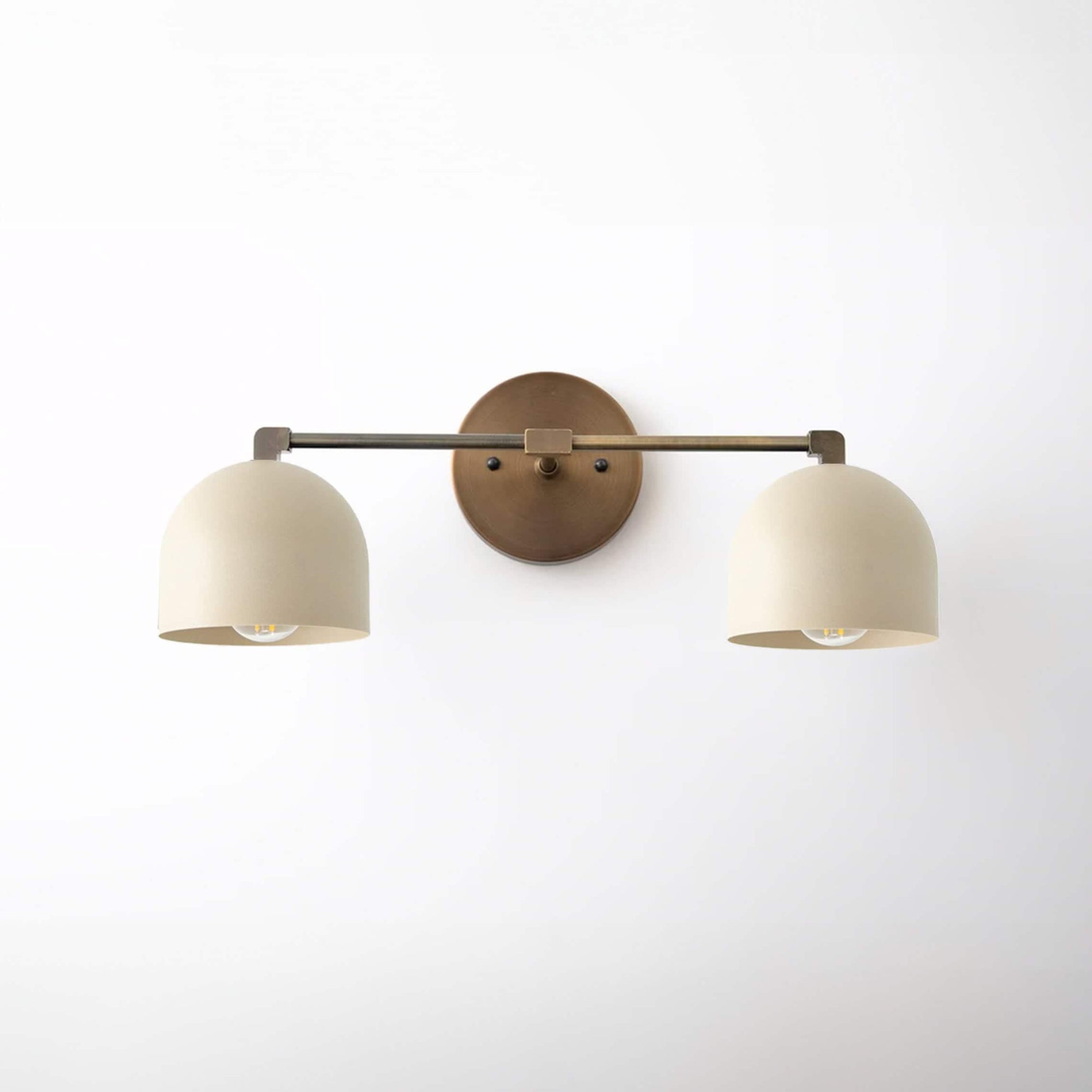 Two-bulb vanity light with cream rounded shades and antique brass finish wall mount and arms. - VANITY LIGHT MODEL NO. 0698