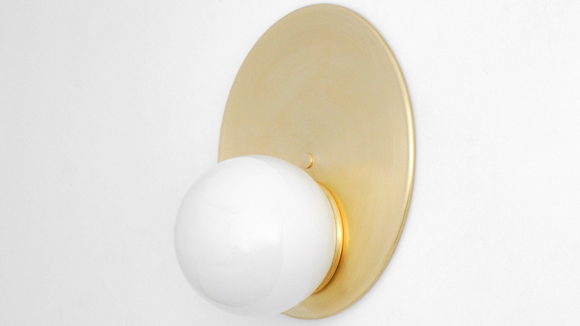 Mid-century modern wall sconce with raw brass circular backplate and white globe shade. - SCONCE MODEL NO. 6703