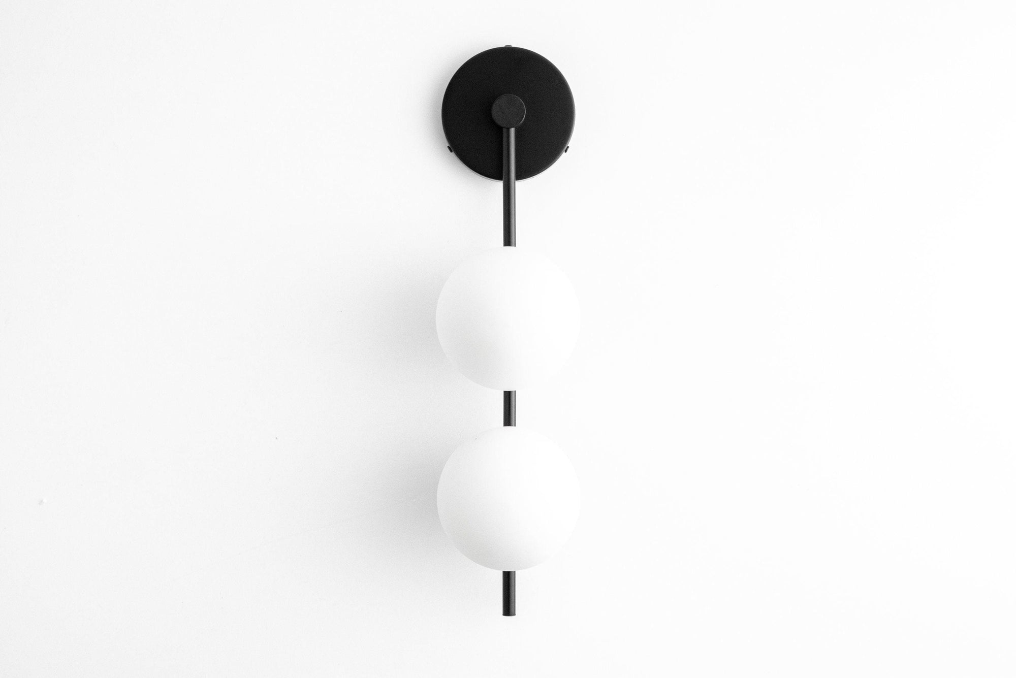 Mid-century modern black metal wall sconce with two white globe glass shades in vertical alignment. - SCONCE MODEL NO. 0344