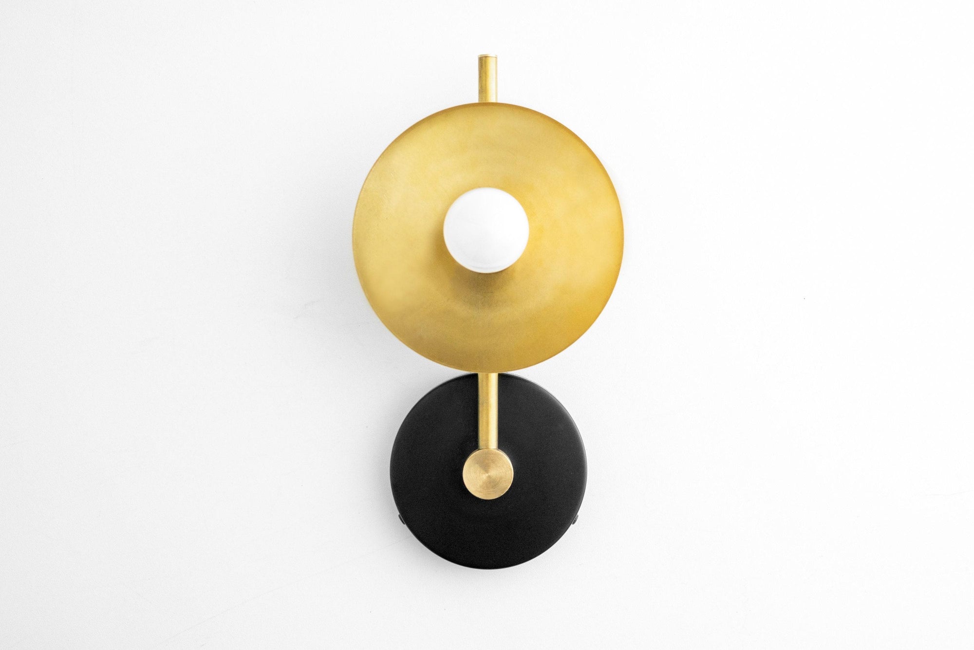 Art Deco wall sconce with black circular base and raw brass disc shade surrounding bare bulb. - SCONCE MODEL NO. 2693