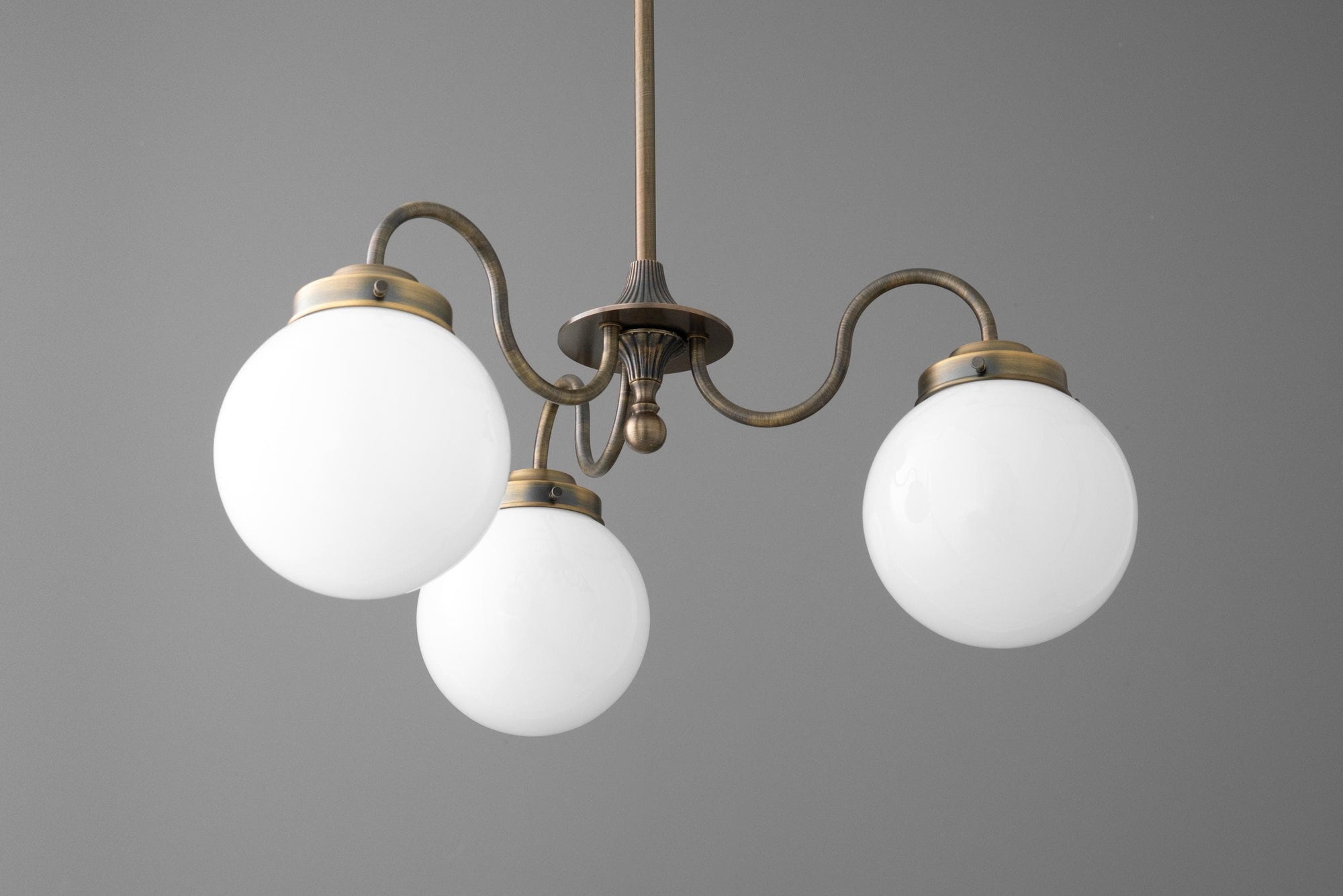 Three-light antique brass chandelier with curved arms and frosted white glass globes on gray background. - CHANDELIER MODEL NO. 5877