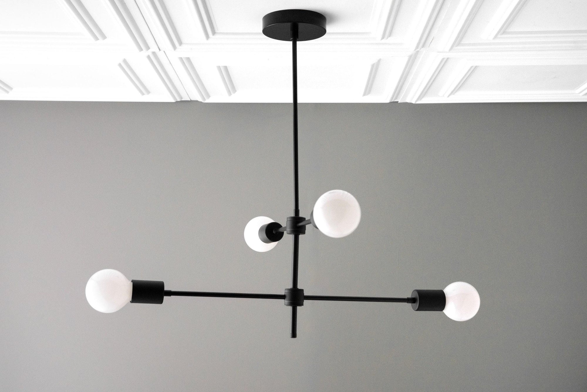 Black metal chandelier with four white globe bulbs arranged in a cross-shaped Art Deco design. - CHANDELIER MODEL NO. 5598